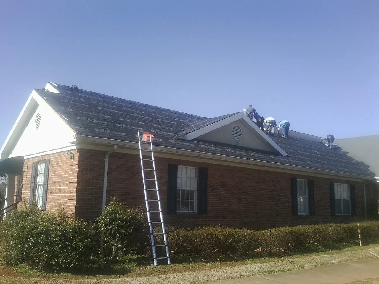Crew tearing shingles off a brick ranch roof with a ladder set — Emergency Roof Repair work by our crew in Seven Springs
