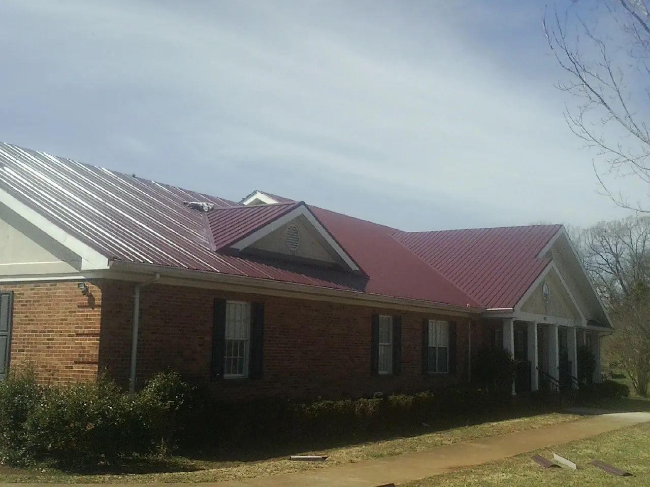 Red metal roof with gabled entries on a long brick building, from a Hail Damage Roof Repair job in Seven Springs