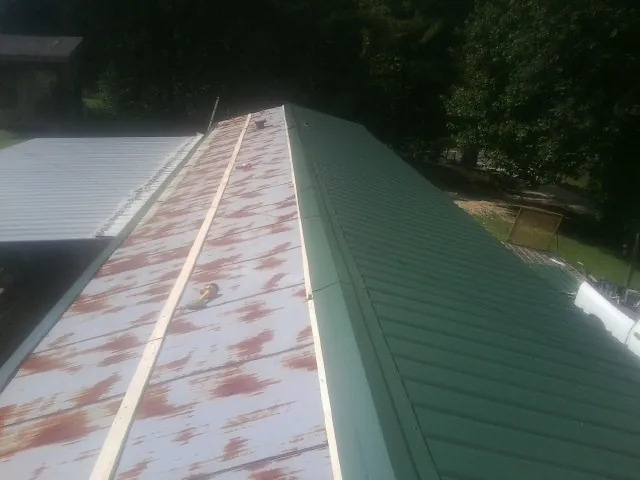 Old rusted panels beside newly installed green metal roofing — Wind Damage Roof Repair by Roofing Brothers in Seven Springs