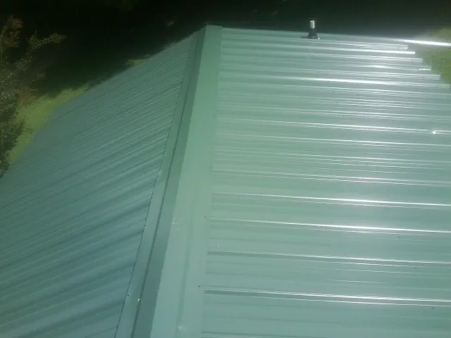 New green metal panels meeting at the ridge of a roof — Flat Roof Repair work by our crew in Seven Springs