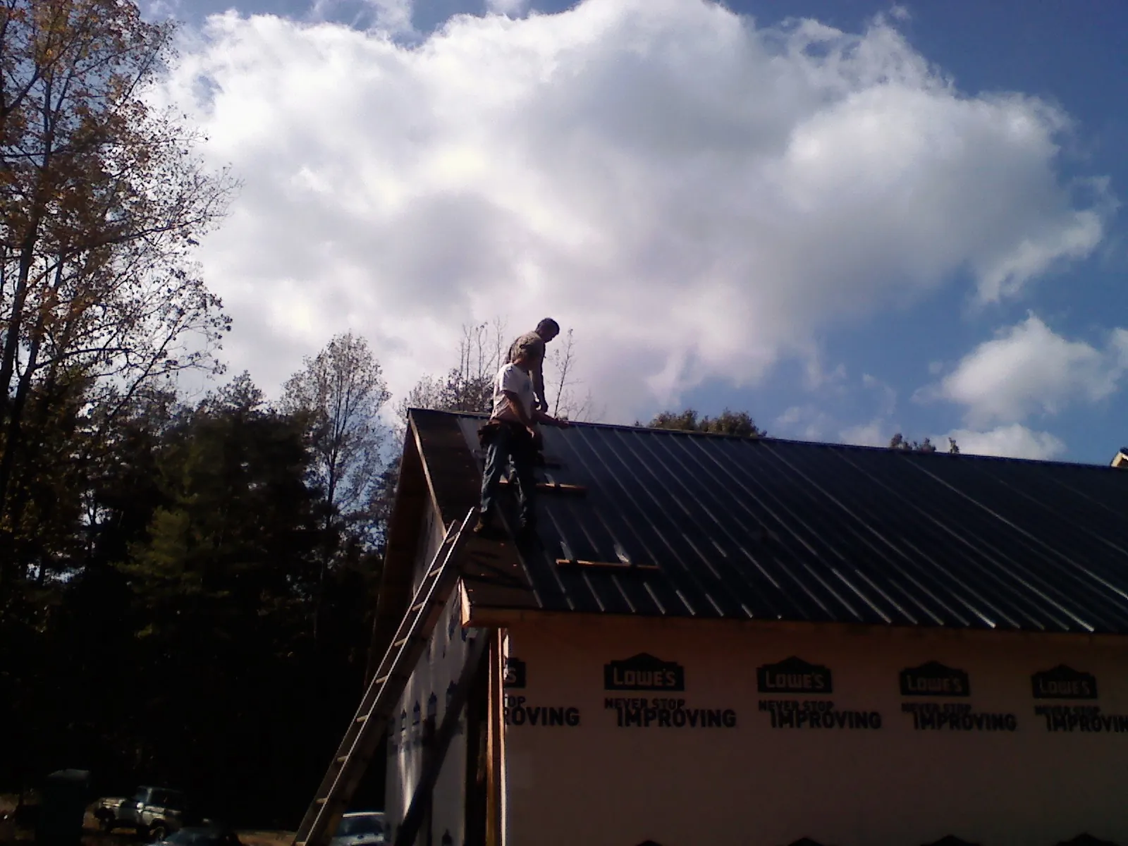 Roofer fastening dark metal panels high against a cloudy sky, from a Roof Inspection job in Seven Springs