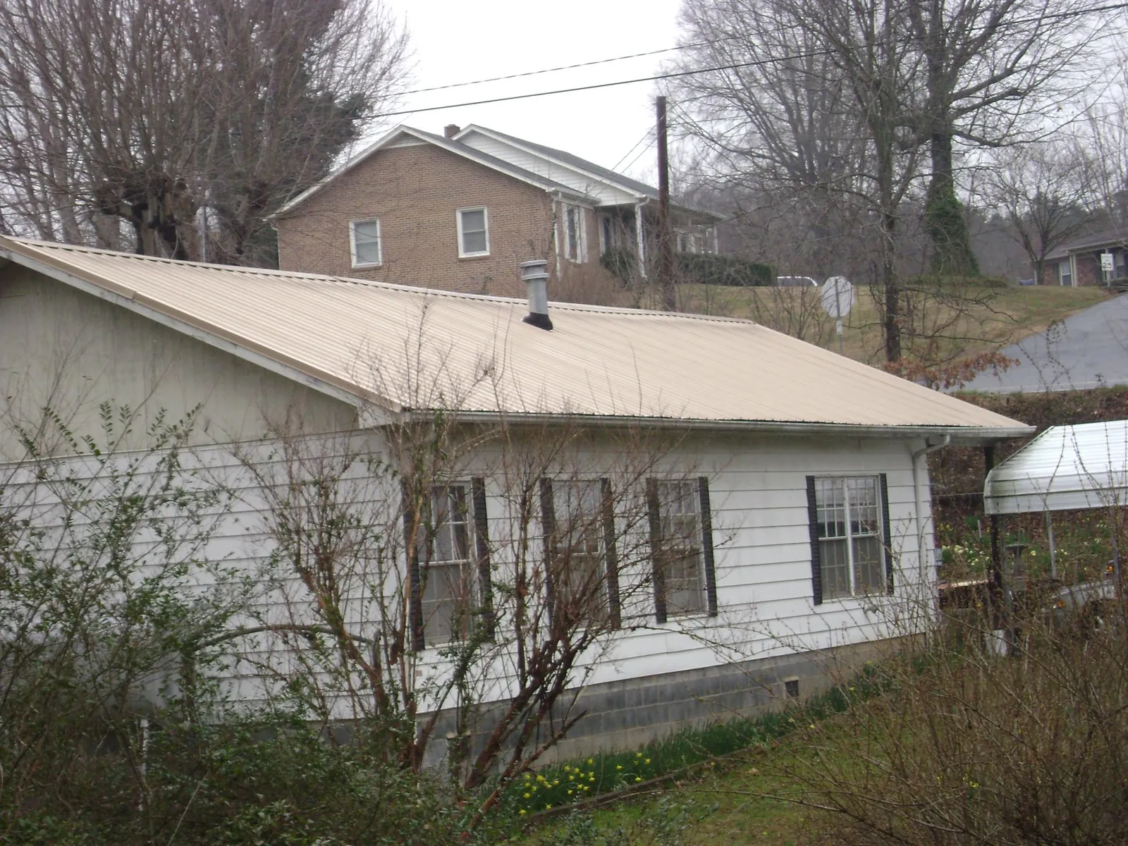 Tan metal roof on a white sided house set into a hillside — Commercial Roofing by Roofing Brothers in Seven Springs