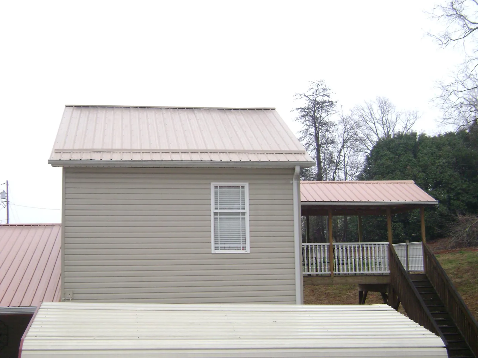 Tan metal roofs on a two story addition and attached porch, from a Roof Replacement job in Seven Springs
