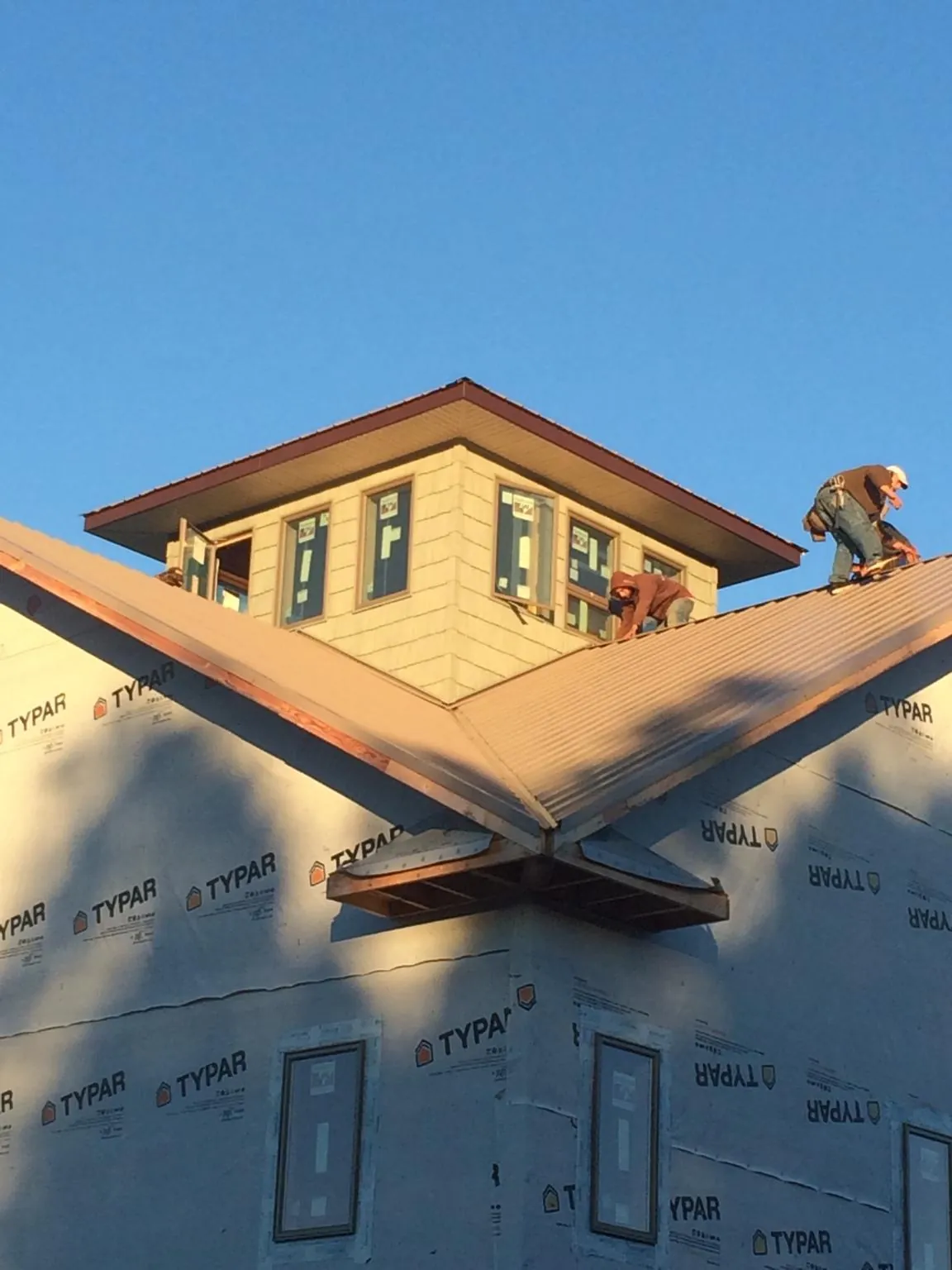 Roofers working around a rooftop cupola on a new metal roof at sunset — Roof Waterproofing in Seven Springs by Roofing Brothers